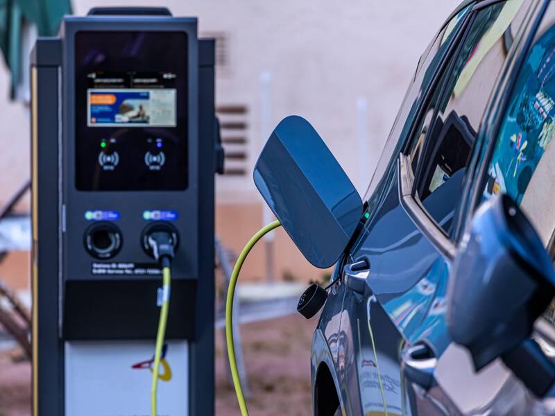 Eine E-Ladestation für Elektroautos. Von der Ladestation führt ein Ladekabel in die Tanköffnung eines grauen Autos.